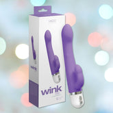 The image features a lavender VeDO Wink Rabbit Vibe vibrator alongside its packaging, which emphasizes the G-Spot and Clitoris Targeted Design. The blurred background with vibrant bokeh lights adds a playful element, accompanied by text showcasing its sophisticated features.